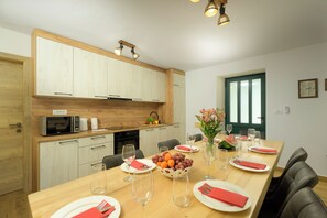 Een moderne keuken met houten kastjes, een magnetron en een eethoek met een lange tafel voor zes personen.