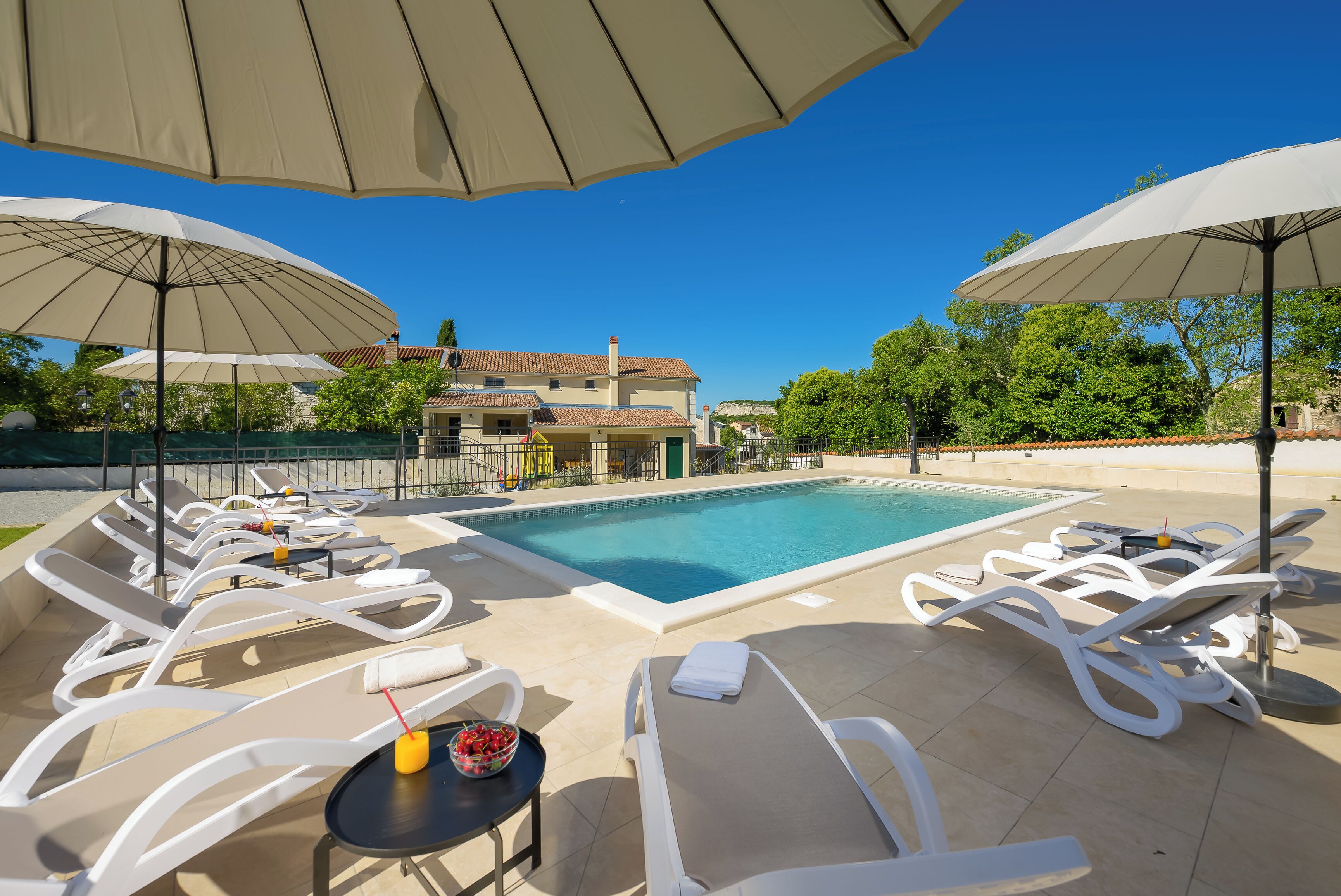 A poolside area with lounge chairs, umbrellas, and a table with a drink.