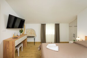 Een slaapkamer met een bed, een bureau, een stoel, een televisie en een raam met gordijnen.