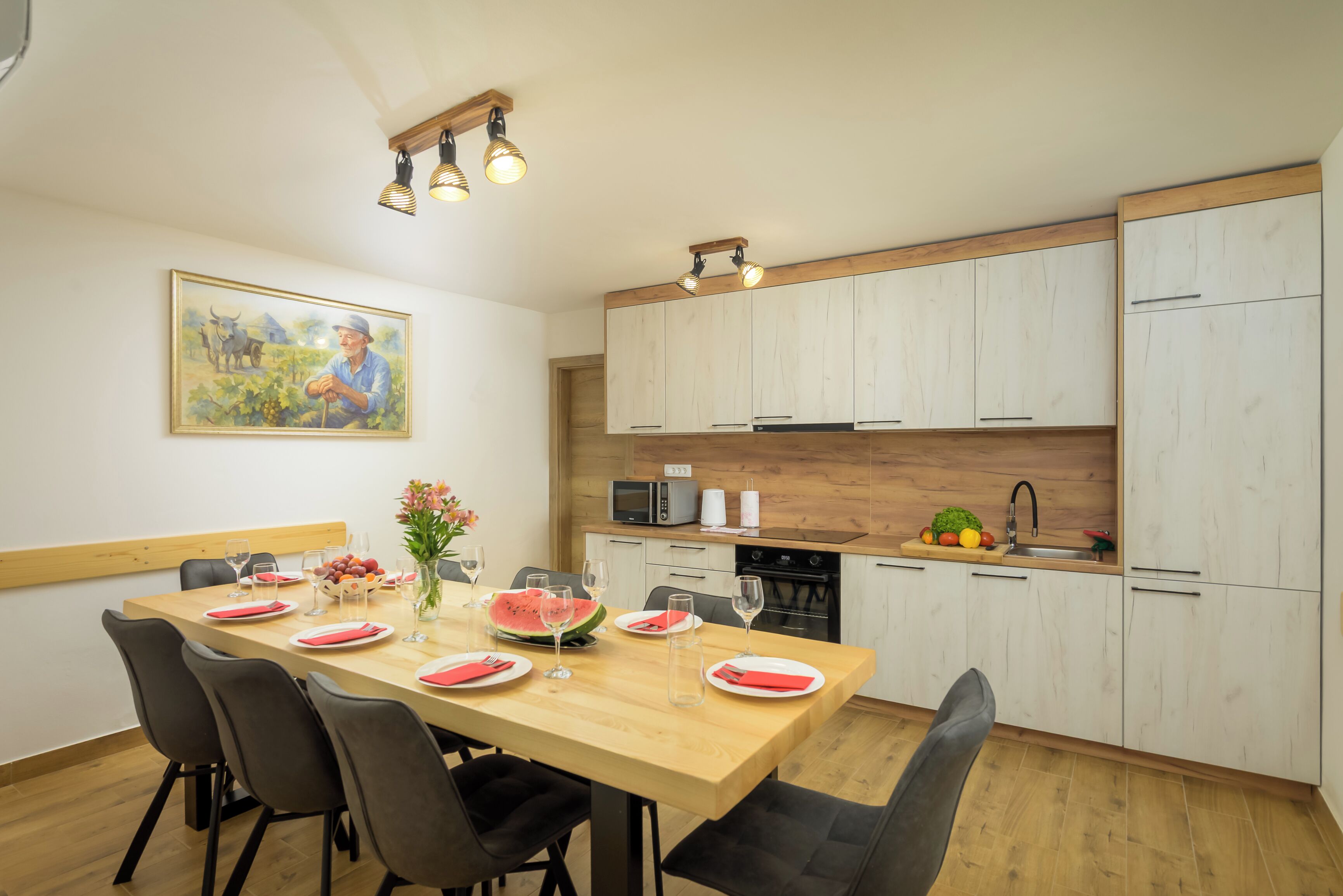 Une cuisine moderne avec des meubles en bois, une table à manger dressée pour quatre personnes et un tableau accroché au mur.