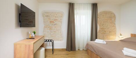 A bedroom with a bed, a desk, a chair, a TV mounted on the wall, and a stone wall.