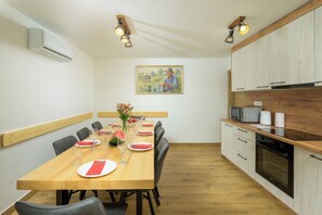 Een eetgedeelte met een houten tafel voor zes personen, een schilderij aan de muur, en een keuken met houten kastjes en apparatuur.