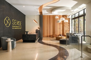 Un hall d’hôtel moderne avec un comptoir d’accueil, un espace salon et de grandes fenêtres.