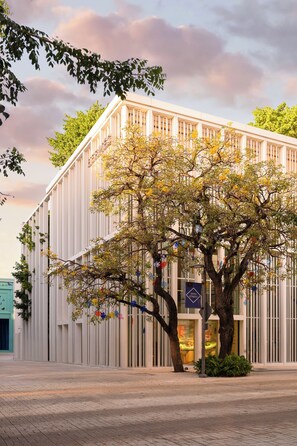Ein modernes Gebäude mit einem großen Baum davor, einem Schild mit einem blauen Pfeil und blauem Himmel.