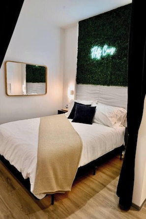 A bedroom with a bed, a mirror, a neon sign, and a green wall.