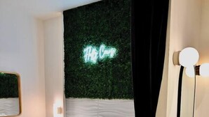 Une chambre à coucher moderne avec un lit, un néon, un miroir et un luminaire fixé au mur.