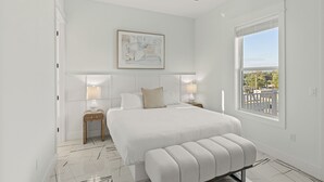 Une chambre à coucher avec un lit, des tables de chevet, un ventilateur de plafond, une fenêtre donnant sur un beau paysage et un tableau accroché au mur.