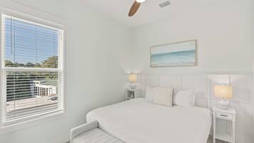 A bedroom with a bed, bedside tables, a ceiling fan, a window with blinds, and a painting on the wall.