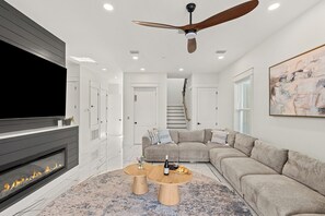 Ein modernes Wohnzimmer mit Kamin, großem Flachbildfernseher, Deckenventilator, Ecksofa und Couchtisch.