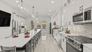Une cuisine moderne dotée d’un îlot central, d’appareils électroménagers en acier inoxydable et de luminaires suspendus.