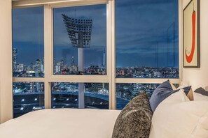 Camera da letto con un'ampia finestra che si affaccia su una vista notturna della città, con un'alta torre e uno stadio.