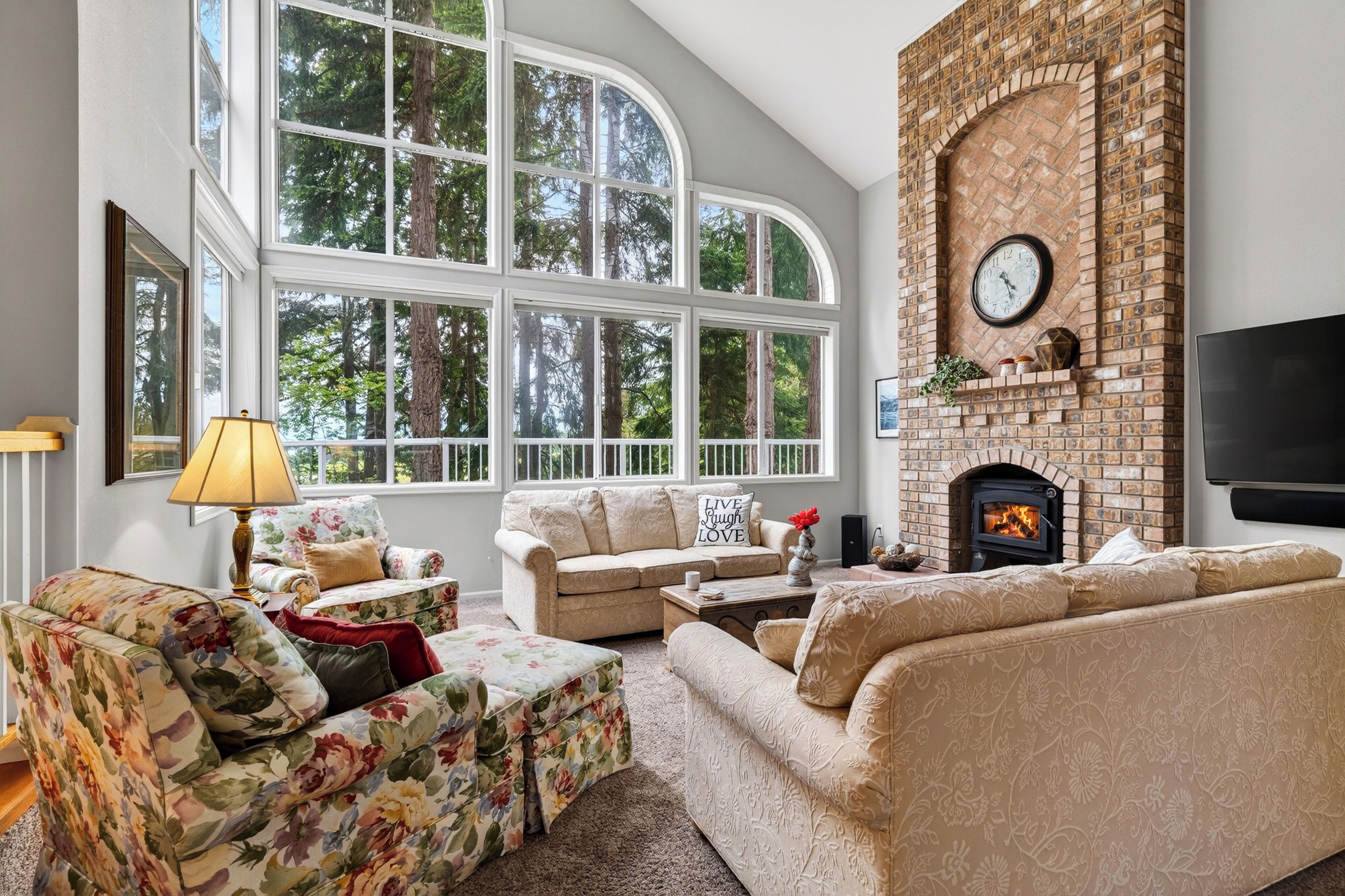 Bright great room with soaring windows, cozy seating, and peaceful wooded views.