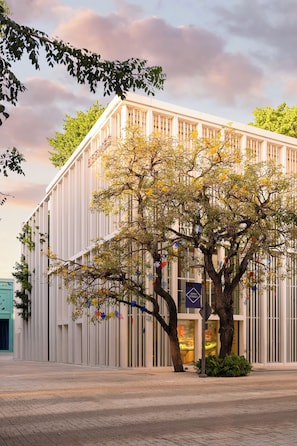 Un bâtiment moderne avec un grand arbre devant, un panneau avec une flèche bleue et un ciel dégagé.