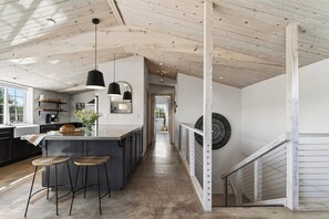 Une cuisine moderne dotée d’un îlot central, de tabourets de bar, de luminaires suspendus et d’un escalier avec une rampe.