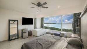 Ein modernes Hotelzimmer mit einem großen Bett, einem Deckenventilator, einem Flachbildfernseher, einer integrierten Badewanne und Blick auf den Ozean.