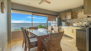 Eine moderne Küche mit Meerblick, ein Essbereich mit Korbstühlen und einem Deckenventilator.