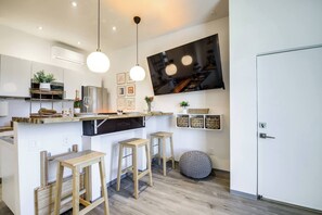 Una cocina moderna con taburetes de madera, un televisor montado en la pared y una puerta blanca.
