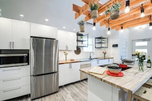 A modern kitchen with stainless steel appliances, wooden ceiling beams, and hanging plants.
