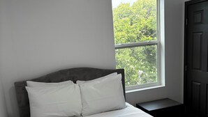 Ein Bett mit weißer Bettwäsche, ein Fenster mit Blick auf Grünflächen und eine dunkle Tür.