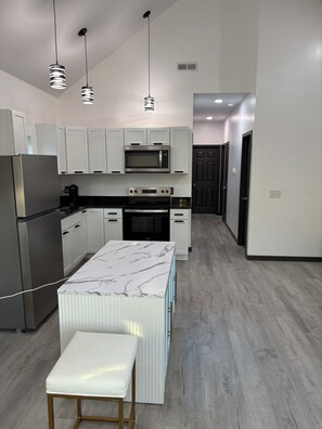Una cucina moderna con mobili bianchi, un piano di lavoro in marmo, forno integrato e frigorifero in acciaio inossidabile.