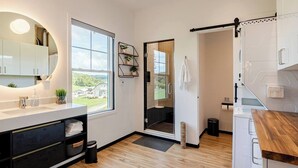 Un baño moderno con ducha, lavamanos e inodoro. Una ventana ofrece vistas al exterior.