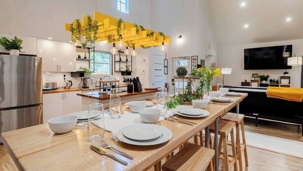 Una cocina moderna con una mesa larga de comedor preparada para cuatro personas, un horno empotrado y un ventanal amplio.