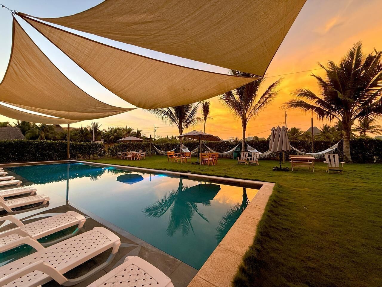 Piscina con sillones de descanso, una hamaca y sombrillas bajo una vela de sombra.