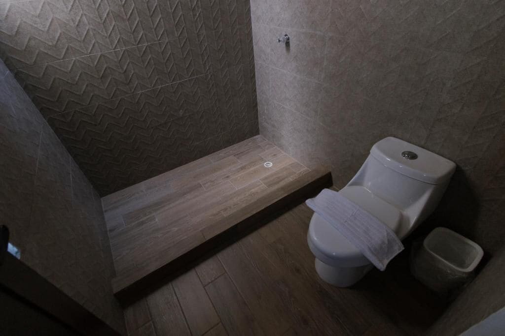 A bathroom with a shower, toilet, and a trash bin.