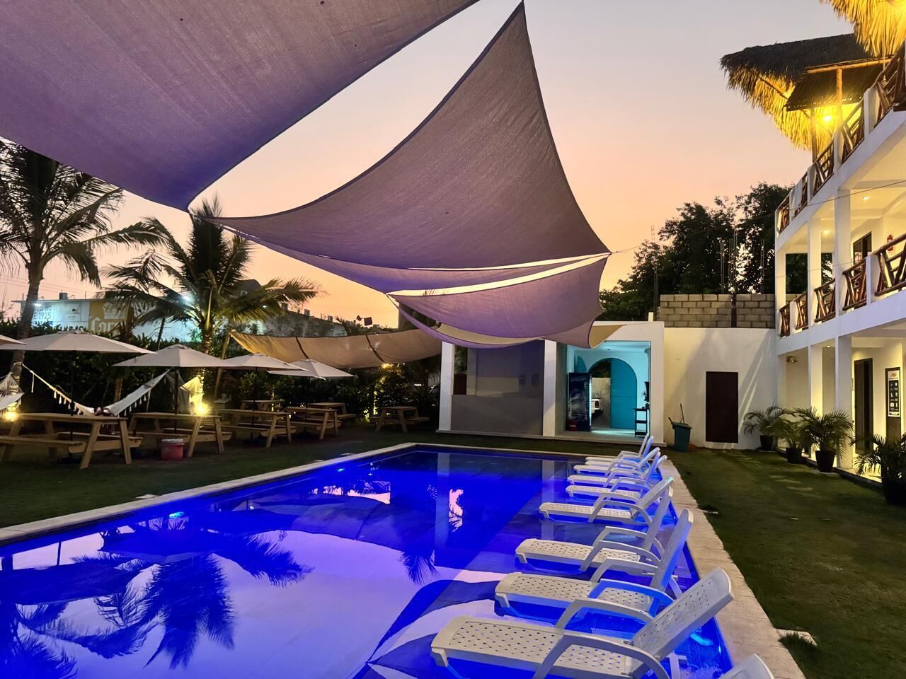 A pool area with lounge chairs, a building with a balcony, and palm trees.