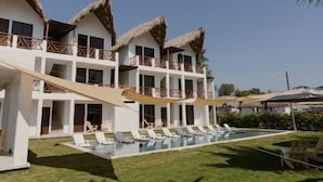 A resort with multiple thatched-roof buildings, a swimming pool, and a well-maintained lawn.