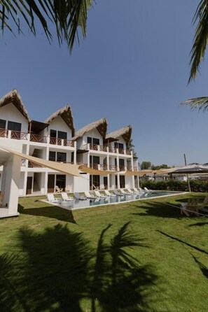 A resort with multiple thatched-roof buildings, a swimming pool, and a well-maintained lawn.