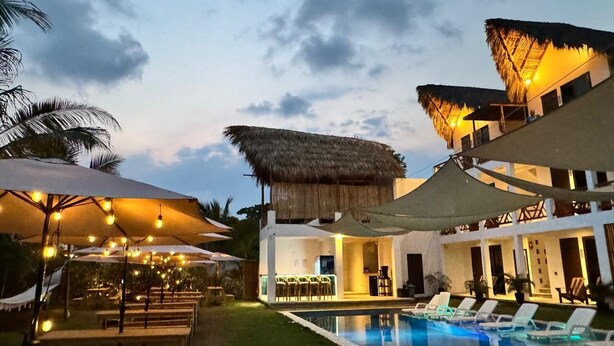 A poolside area with lounge chairs, umbrellas, and a building with a thatched roof.