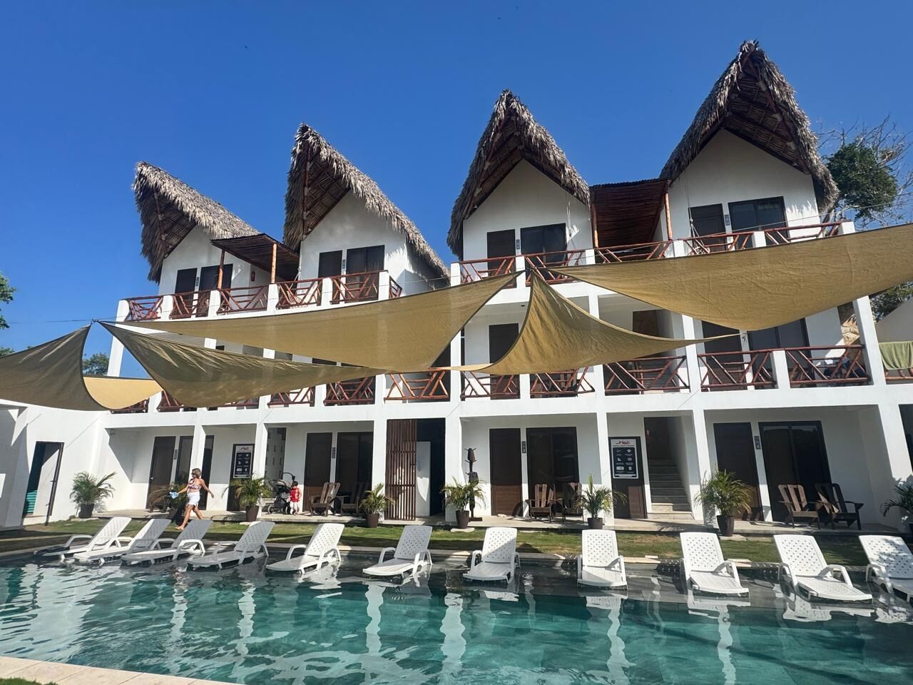 Un resort con piscina, edificios de techo de paja y tumbonas.