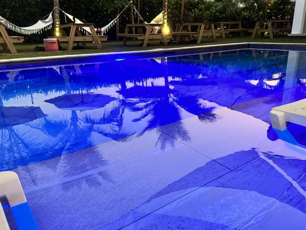 Una piscina con superficie blu trasparente, sedie a sdraio in legno e un'amaca.