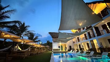 Zona de piscina en un resort, con sombrillas, sillas de descanso y un edificio con balcones.