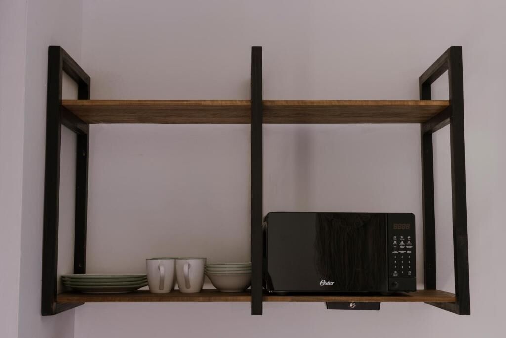 A kitchen with a microwave on a shelf, a wooden shelf, and some dishes.