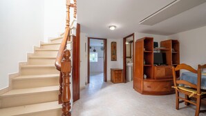 Eine Treppe mit Holzbalkonen, ein Holzstuhl, ein Fernseher auf einem Holzständer und ein Fliesenboden.