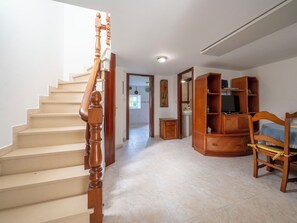 Eine Treppe mit Holzbalkonen, ein Holzstuhl, ein Fernseher auf einem Holzständer und ein Fliesenboden.