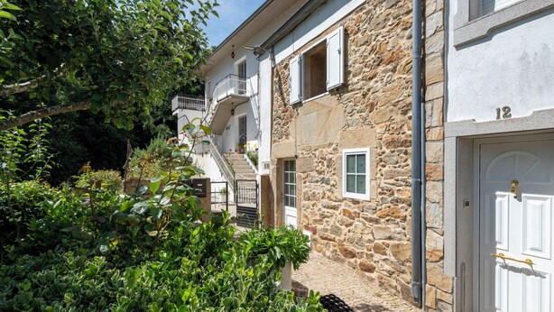 Ein Steinhaus mit weißer Tür, einer Treppe und einem Garten.