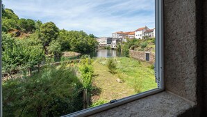Ein Fluss mit Häusern an einem Hügel, betrachtet durch ein Fenster.