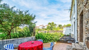 Eine Terrasse mit rundem Tisch und Stühlen, eine Steinmauer und ein Blick auf Häuser im Hintergrund.