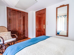 Ein Schlafzimmer mit einem Bett, einem Sessel, zwei Holztüren und einem Spiegel an der Wand.