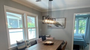 Un comedor con una mesa de madera, sillas, un banco con cojines, una lámpara colgante y vistas amplias a través de grandes ventanales.