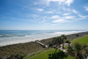 Vista costera con playa, un muelle de madera y vegetación escasa.