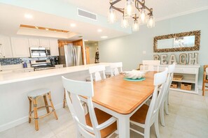 A modern kitchen with white cabinets, a wooden dining table, and a chandelier. - Amazing 4th floor 3/2 condo at Sand Dollar Unit 3-407! (St. Augustine)