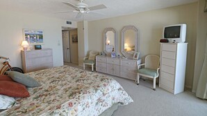 Un dormitorio con cama, cómoda, silla, televisor y ventilador de techo.