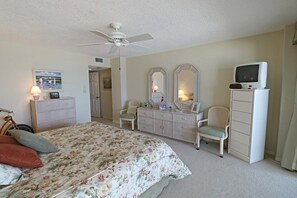 A bedroom with a bed, dresser, chair, television, and ceiling fan. - Incredible Direct Oceanfront Views from 6th Floor Balcony at Sand Dollar 3-604 (St. Augustine)