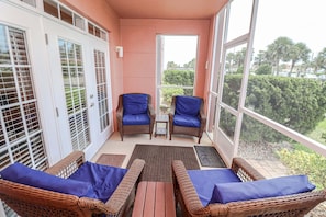 A balcony with wicker furniture, a small table, and a view of greenery. - Updated, spacious 3/2 in Gated Seaside at Anastasia A103 (St. Augustine)