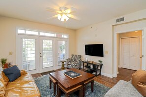 A living room with a sofa, coffee table, patterned armchair, television, and a door. - Updated, spacious 3/2 in Gated Seaside at Anastasia A103 (St. Augustine)