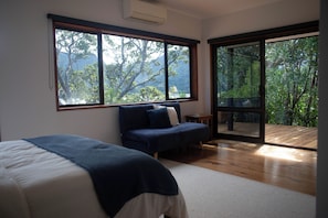 Ein Schlafzimmer mit Bett, einer Couch, großen Fenstern und Blick auf Bäume.